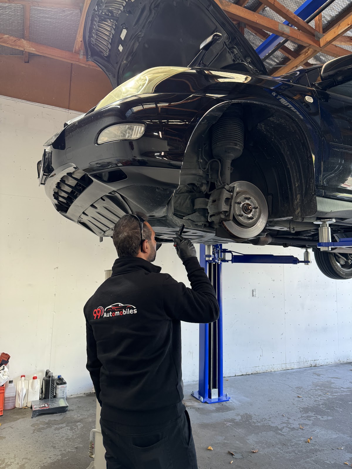A 99 Automobiles mechanic inspecting a car on the hoist